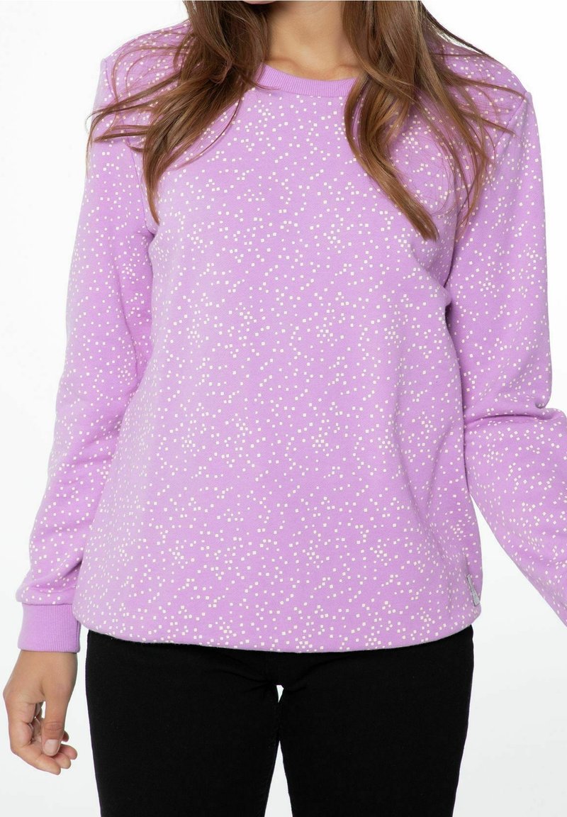 Maglione viola con pois bianchi; maniche lunghe, polsini e scollatura a coste, texture morbida, vestibilità comoda. Indossato con pantaloni neri.