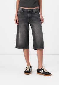Black, knee-length denim culottes with a faded finish, front pockets, and a button closure, paired with black and white sneakers.