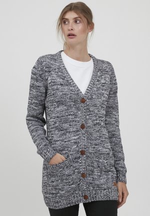Cardigan en tricot dans un motif noir et blanc chiné, avec un décolleté en V profond, six boutons marron et deux poches avant.