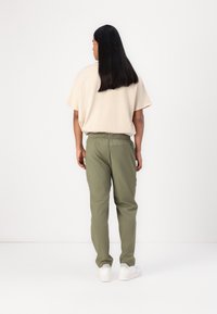 Beige oversized t-shirt met opgerolde mouwen, gecombineerd met lichtgewicht olijfgroene broek, elastische tailleband en zakken. Witte sneakers maken de look af.