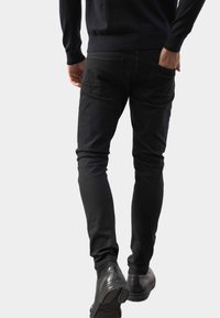 Czarne slim-fit dżinsy o gładkiej strukturze, z dwoma tylnymi kieszeniami, w zestawieniu z czarnymi butami i ciemnym swetrem.