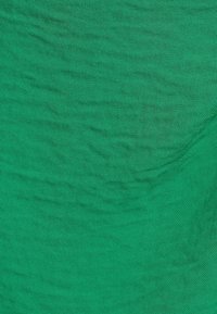 Vihreä kangas, jossa on hieman teksturoitu pinta, joka näyttää hienovaraisia sävyvaihteluita ja tasaisen kudontakuviot koko ajan.