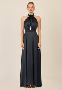 Abito nero senza spalline in satin, con un'apertura a chiave frontale e un'accenno di fiore all'collo, e una gonna lunga e fluente.