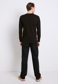 Sort langærmet skjorte lavet af bomuld, kombineret med mørke bukser. Skjorten har rund hals og slim fit, med minimal detaljer.