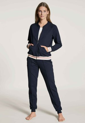 Marine blauwe zip-up jas en bijpassende broek. De jas heeft gestreepte manchetten en zakken; de stof lijkt glad en heeft een relaxte pasvorm.