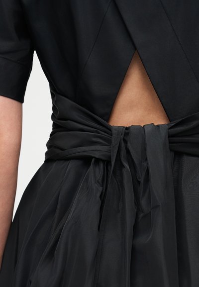 Back view of black dress with short sleeves, open triangular back detail, and wide sash tied in a bow at the waist.