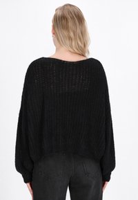 Pulover negru tricotat, cu o croială lejeră, mâneci largi și o textură ribbed. Prezintă un decolteu larg și o lungime scurtă.
