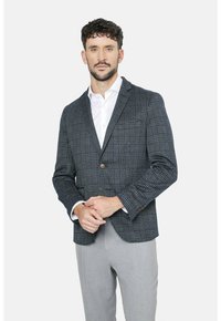 Blazer a cuadros en navy y gris con un corte ajustado, que cuenta con un cierre de dos botones, tejido texturizado y detalles en botones marrones, combinado con una camisa blanca.