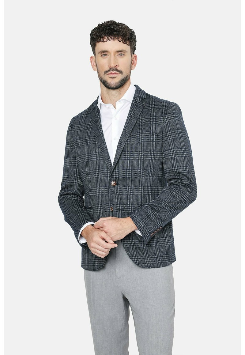 Blazer a cuadros en navy y gris con un corte ajustado, que cuenta con un cierre de dos botones, tejido texturizado y detalles en botones marrones, combinado con una camisa blanca.