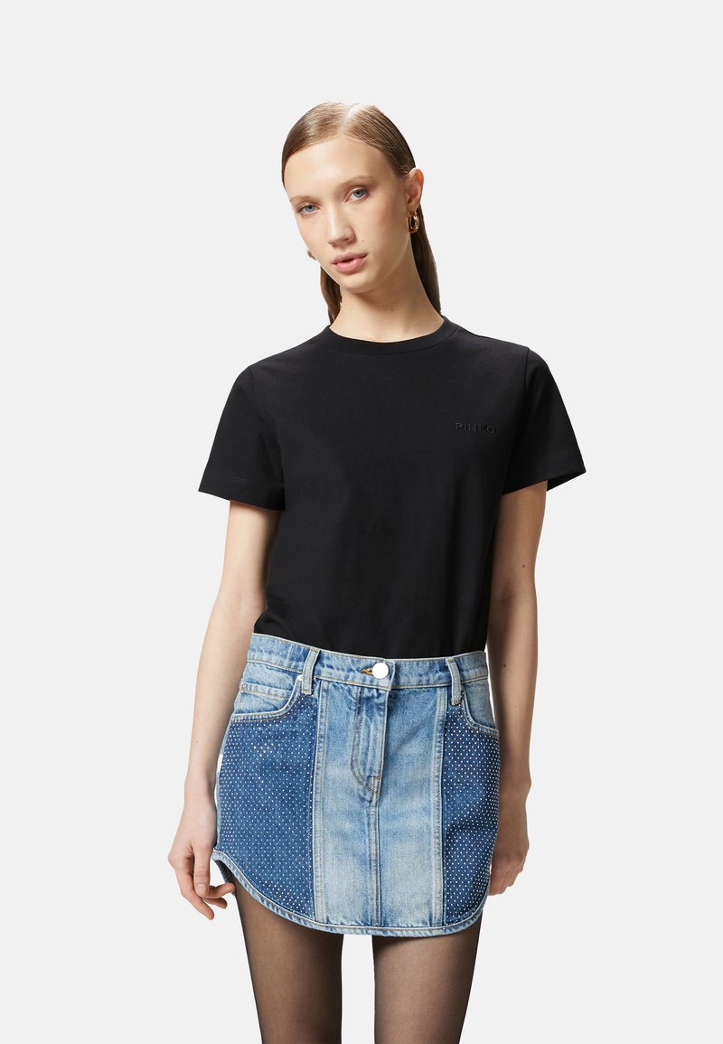 T-shirt in cotone nero con un logo sottile, abbinato a una mini gonna di jeans con diverse sfumature di blu e dettagli in tessuto a pois.