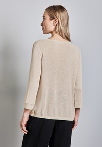 Maglione beige a maglia con vestibilità ampia, maniche a tre quarti e scollatura larga. Tessuto strutturato con un design casual, abbinato a pantaloni neri.