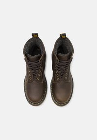 Botine din piele maro cu un finisaj texturat, căptușeală din fleece gri, cusături galbene și design cu șireturi. Au un tab de tragere pe guler.