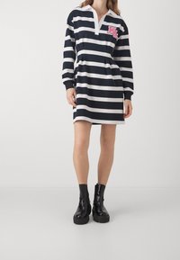 Marinblå och vit randig klänning med krage, långärmad och med en framficka med "KL"-logotyp. Matchad med svarta stövlar.