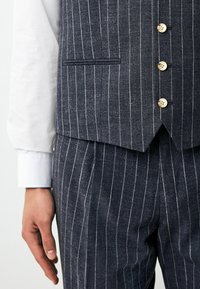 Navy striped vest with light pinstripes, three buttons, and a narrow pocket, paired with matching trousers and a white shirt cuff.