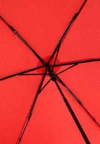 Red umbrella viewed from underneath, featuring a smooth fabric texture, black metal frame, and prominent rib structure extending outward.