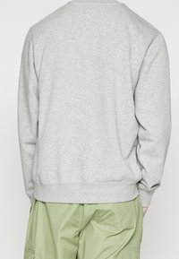 Grå sweatshirt med rund halsringning och ribbad fåll, med långa ärmar och ett mjukt, texturerat tyg. Matchad med ljusgröna byxor.