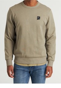 Felpa khaki, colletto a giro, polsini e orlo a costine, piccolo logo nero ricamato sul petto, texture morbida, abbinata a jeans blu.