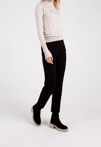 Jasnoróżowy dopasowany top z długim rękawem i golfem z detalami szwów, zestawiony z czarnymi wąskimi spodniami i czarnymi botkami z beżowymi podeszwami.