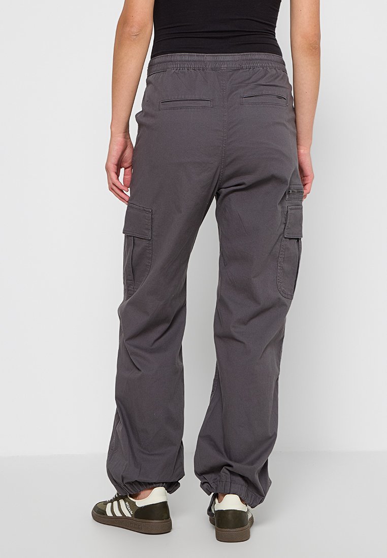Szare spodnie cargo z elastycznym paskiem w talii, dwiema bocznymi kieszeniami i regulowanymi mankietami. Wykonane z trwałego materiału o gładkiej teksturze.