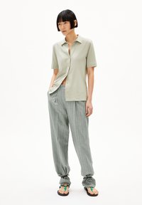 Camicia verde chiaro a maniche corte con collo, abbinata a pantaloni grigi a righe sottili e larghi. Sandali con cinturini verdi.