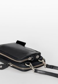 Schwarze Leder-Umhängetasche mit silbernen Reißverschlüssen, abnehmbarem Tragegurt und glatter Textur. Kompaktes Design mit funktionalen Hardware-Akzenten.