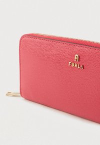 Koralfarvet læderpung med en tekstureret finish, med et guldfarvet "FURLA"-logo og en lynlåslukning langs den øverste kant.