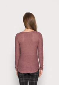 Maglia a maniche lunghe in punto maglia color malva, con scollo rotondo e polsini a coste. Il tessuto ha un aspetto leggero e strutturato.