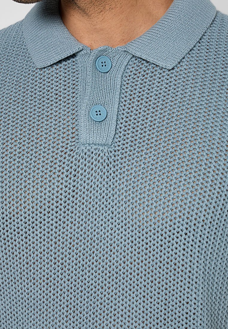 Hellblaues gestricktes Poloshirt mit strukturiertem Gewebe, einem Kragen und zwei passenden Knöpfen an der Knopfleiste.