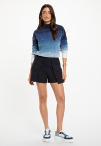 Maglione blu a ombre con collo alto, abbinato a pantaloni cargo blu scuro con due tasche frontali. Sneakers bianche con accenti blu.