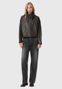 Brūns ādas īss jaka ar augstu apkakli, saskaņota ar brīviem melniem džinsiem. Gluda tekstūra, minimāla aparatūra un nav redzamu rakstu.