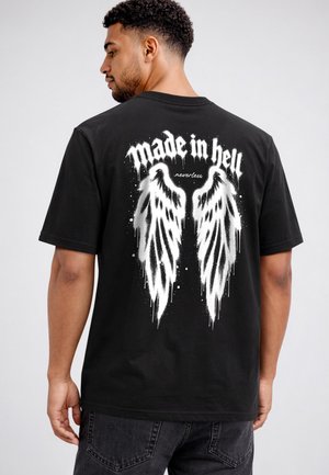 Mann trägt schwarzes T-Shirt mit weißen Graffiti-Engelsflügeln und dem Text "made in hell nevertheless" auf dem Rücken.