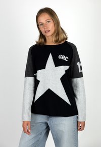 Black and grey sweater with a large white star design, featuring the text "GRC" and "12." Made from a soft, knitted material.