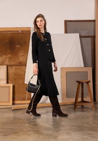 Čierny pletený kardigán so zlatými gombíkmi, skombinovaný s rovnakou čiernou sukňou. Nosený s tmavohnedými čižmami po kolená a malou čiernou kabelkou.