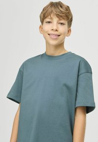 Tričko s crew neck v tyrkysové barvě, krátké rukávy, uvolněný střih, hladká bavlněná tkanina, minimalistický design bez viditelných vzorů nebo akcentů.