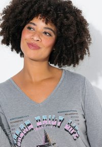 Grijze V-hals T-shirt met een grafische print van de woorden "Urban Daily Life," inclusief kleurrijke accenten en een ster ontwerp. Glad textuur.