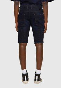Shorts de mezclilla azul oscuro de corte recto, con dos bolsillos traseros y costuras en contraste. Combinados con zapatillas altas negras.
