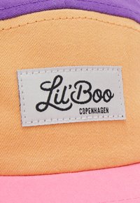 Värviline müts, millel on oranžid, roosad ja lillad paneelid. Tekstureeritud kangas, millel on tikitud silt, kus on mustlas kirjas "Lil' Boo Copenhagen".