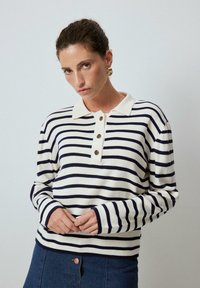 Randig långärmad polo i kräm och marin, med en knappslå och ribbade ärmar, tillverkad av mjukt material med en avslappnad passform.