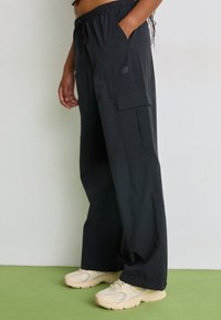 Schwarze Cargo-Hose aus leichtem Stoff mit lockerer Passform, ausgestattet mit Seitentaschen und einem elastischen Taillenbund. Kombiniert mit beigen Sneakers.