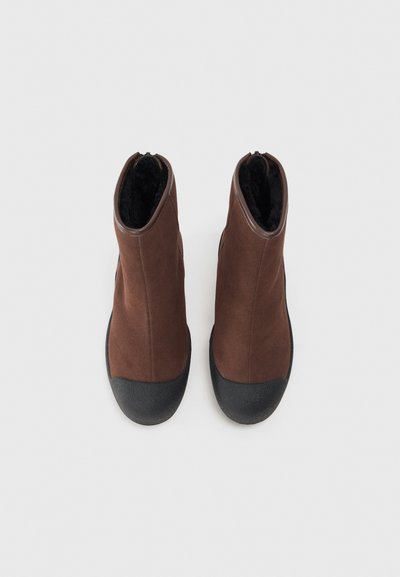 Bottines en daim brun avec un embout en caoutchouc noir et une semelle texturée noire, dotées d'une doublure intérieure douce noire et d'un liseré lisse brun.