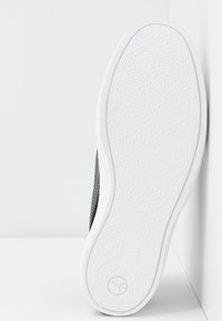 Svart sneakersula med texturerat vitt gummi, som har en slät kant och en cirkulär logotyp präglad i mitten.