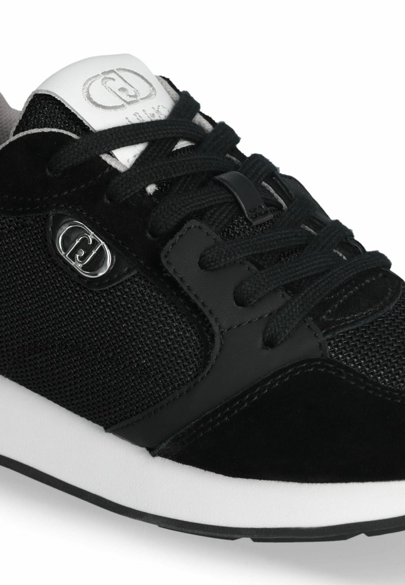Sneaker nera che presenta una combinazione di materiali in rete e suede, lacci tondi, una linguetta imbottita bianca e una suola in gomma testurizzata.