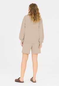Beige sweatshirt och matchande shorts gjorda av mjukt tyg, med avslappnad passform och ribbade ärm- och benavslut. Bruna slidesandaler fulländar outfiten.