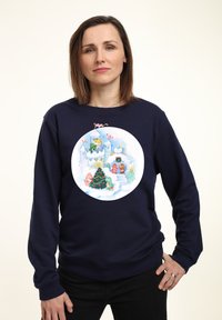 Námořnická modrá mikina s kulatým, barevným vánočním motivem, na němž se nachází hrad, vánoční stromeček a hraví postavy.