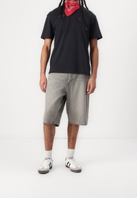 Camiseta de algodón negra con mangas cortas, pantalones cortos de mezclilla gris y zapatillas blancas con acentos negros. Pañuelo rojo alrededor del cuello.
