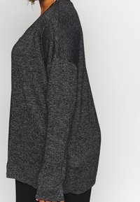 Maglione grigio scuro a maniche lunghe con vestibilità ampia, in tessuto a maglia testurizzato e scollatura rotonda. Presenta spalle cadenti e un orlo curvo.