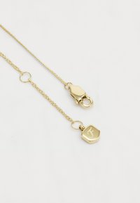 Collier en plaqué or avec une chaîne tressée, fermeture à clip, et un charm hexagonal avec une lettre gravée.