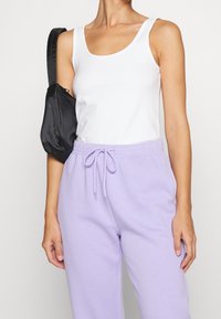 White fitted tank top paired with light purple sweatpants featuring an elastic waistband and drawstring. A small black satin bag is worn.