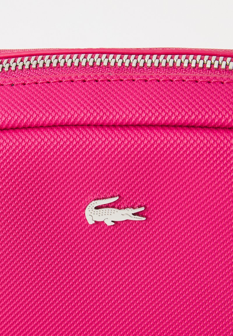 Heldere roze textiele tas met een zilveren krokodillenlogo en een zilveren rits aan de bovenkant.
