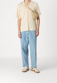 Camisa polo de manga corta beige con un bolsillo en el pecho, pantalones vaqueros holgados de color azul claro, bolso cruzado beige y zapatillas blancas con detalles en marrón.